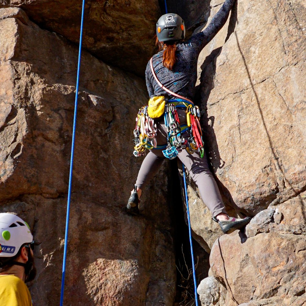 Beginner trad climber undertaking a mock lead climb with a safety top rope during our Learn to Lead Trad climbing course.